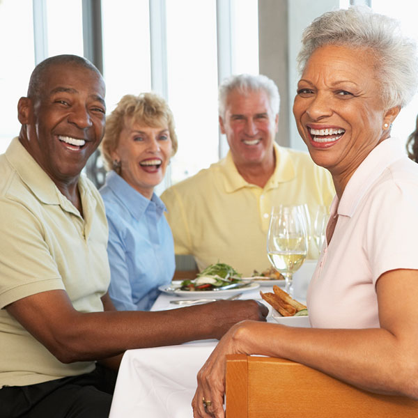 four seniors sitting at a table smiling at the camera with white table cloth and wine glasses