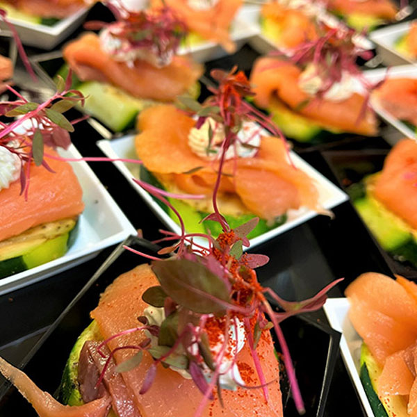 square photo close up of a salmon bite appetizer on white plate and black table