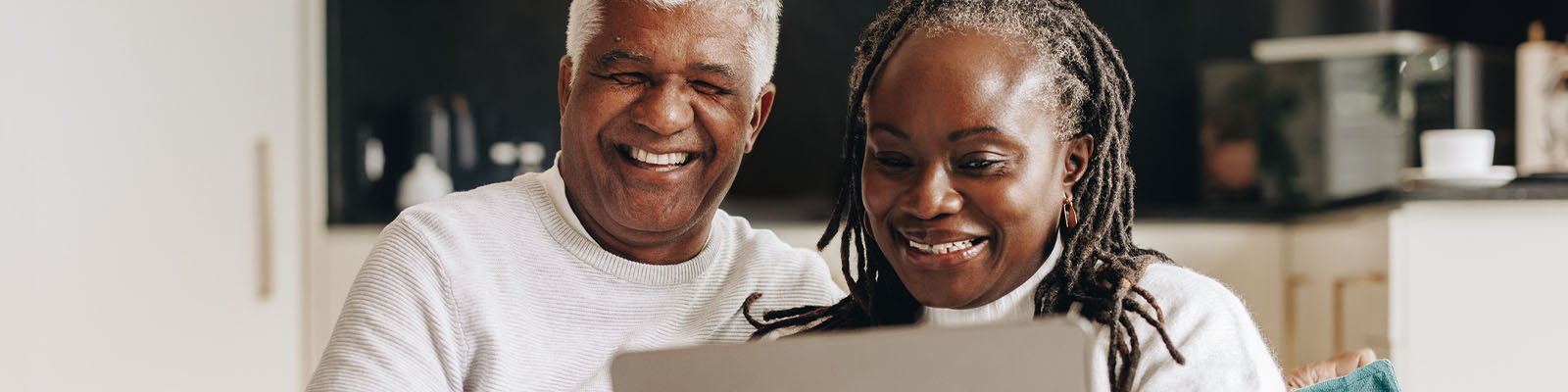 A senior man and senior woman sitting together on a couch looking down at a laptop