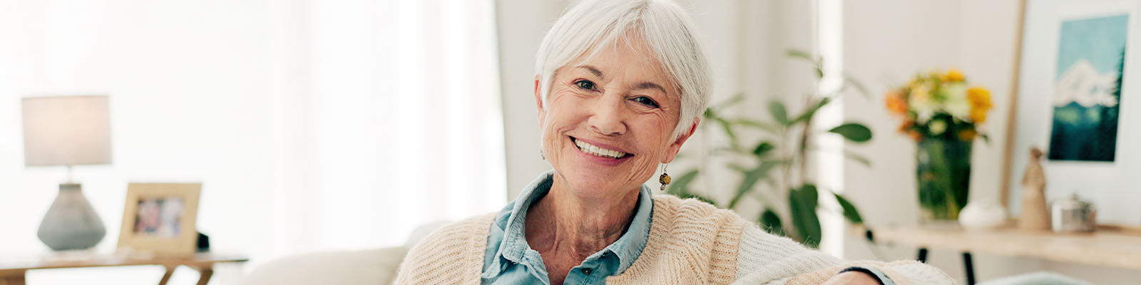 A senior woman with white hair sitting on the couch smiling in her senior independent living residence